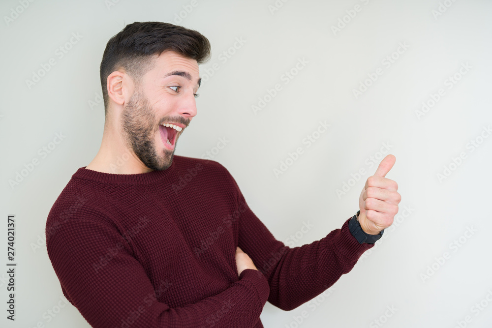 Young handsome man wearing a sweater over isolated background Looking proud, smiling doing thumbs up gesture to the side Young handsome man wearing a sweater over isolated background Looking proud, smiling doing thumbs up gesture to the side
