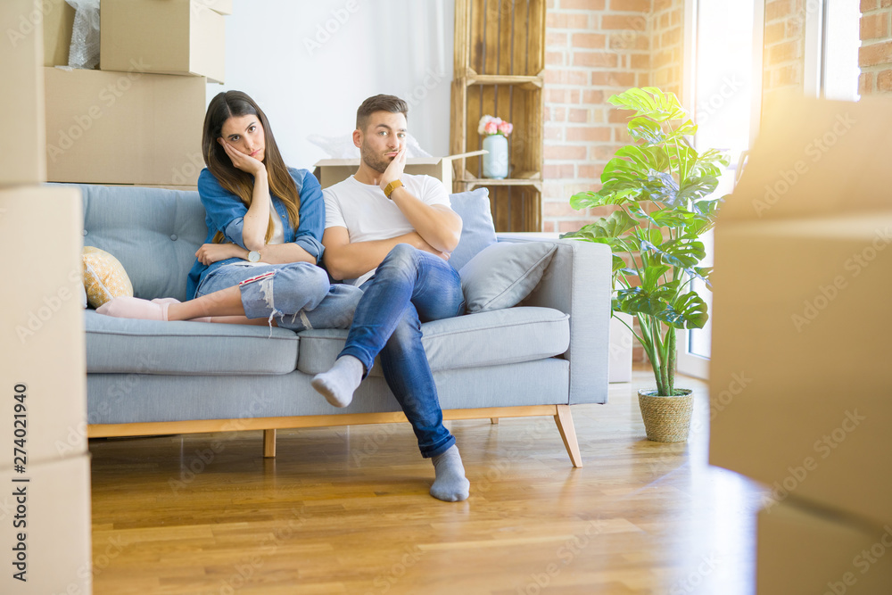 Young beautiful couple relaxing sitting on the sofa around boxes from moving to new house thinking looking tired and bored with depression problems with crossed arms. Young beautiful couple relaxing sitting on the sofa around boxes from moving to new house thinking looking tired and bored with depression problems with crossed arms.