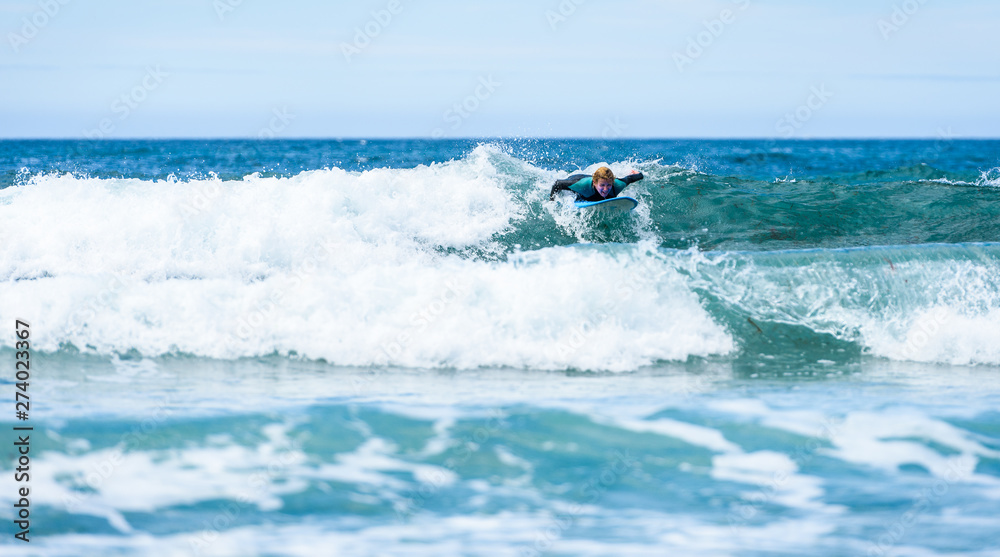 Surfer woman with surfboard is paddling on the wave.