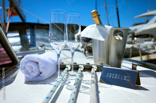 Romantic luxury evening on cruise yacht with champagne setting. Empty glasses and bottle with champagne and tropical sunset with sea background