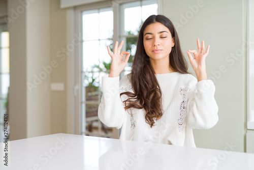 Young beautiful woman at home on white table relax and smiling with eyes closed doing meditation gesture with fingers. Yoga concept.