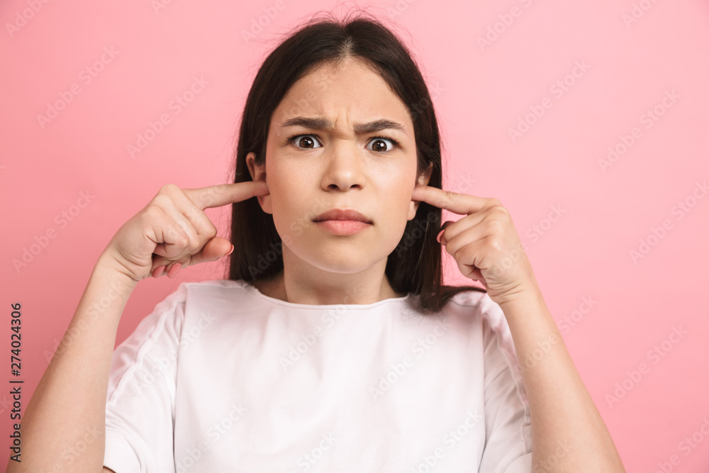 Portrait closeup of sad teenager girl in casual wear looking at camera and plugging her ears with fingers Portrait closeup of sad teenager girl in casual wear looking at camera and plugging her ears with fingers