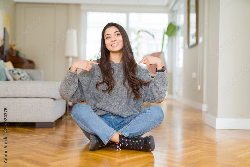 Young beautiful woman sitting on the floor at home looking confident with smile on face, pointing oneself with fingers proud and happy. Young beautiful woman sitting on the floor at home looking confident with smile on face, pointing oneself with fingers proud and happy.