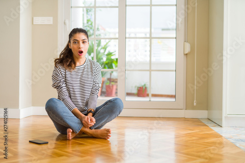 Young beautiful woman sitting on the floor at home afraid and shocked with surprise expression, fear and excited face. © Krakenimages.com
