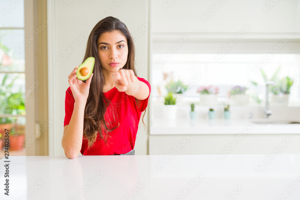 Young woman eating healthy avocado pointing with finger to the camera and to you, hand sign, positive and confident gesture from the front Young woman eating healthy avocado pointing with finger to the camera and to you, hand sign, positive and confident gesture from the front