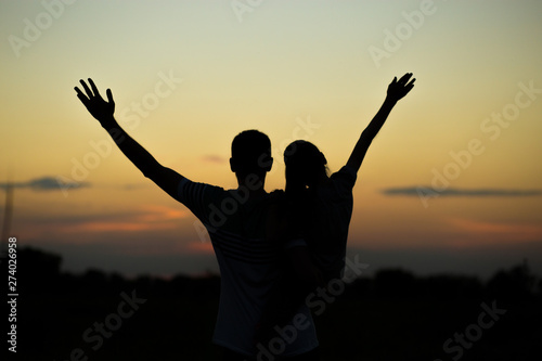 Silhouettes of father and daughter on his shoulders with hands up having fun, against sunset sky. Parenthood, family activities, beach holiday and vacation, support and love themes