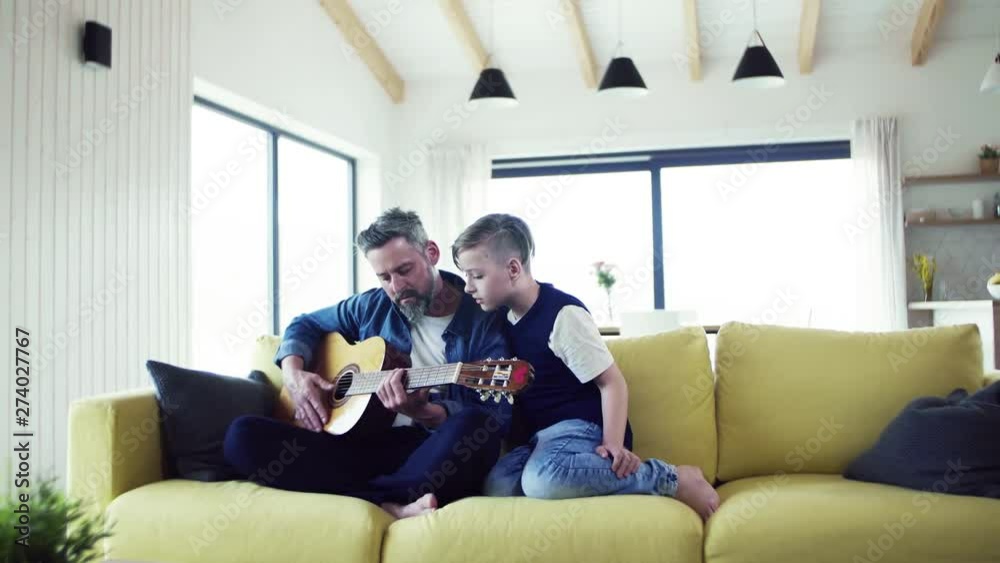 Mature father with small son sitting on sofa indoors, playing guitar. Mature father with small son sitting on sofa indoors, playing guitar.