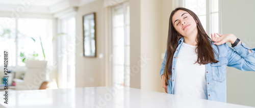 Wide angle picture of beautiful young woman sitting on white table at home stretching back  tired and relaxed  sleepy and yawning for early morning