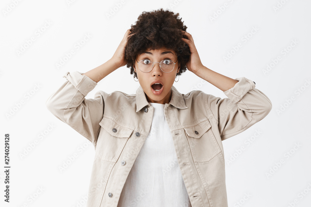 Studio shot of impressed and surprised emotive african american in glasses and beige boyish shirt holding hand on head gasping and smiling broadly being amazed and astonished of recent news