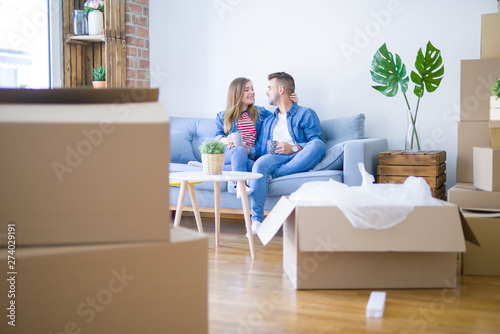 Young couple relaxing drinking a cup of coffee sitting at sofa of  new home with cardboard boxes around them, very happy moving to a new apartment