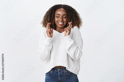 Excitement, anticipation surprise concept. Charming smiling happy african-american young woman cross fingers good luck closed eyes smiling gladly make wish dream party went well, white background photo