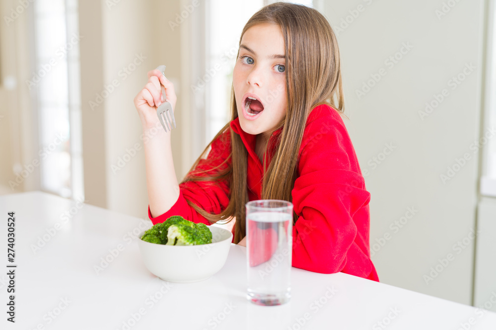 Beautiful young girl kid eating fresh broccoli and drinking water scared in shock with a surprise face, afraid and excited with fear expression Beautiful young girl kid eating fresh broccoli and drinking water scared in shock with a surprise face, afraid and excited with fear expression