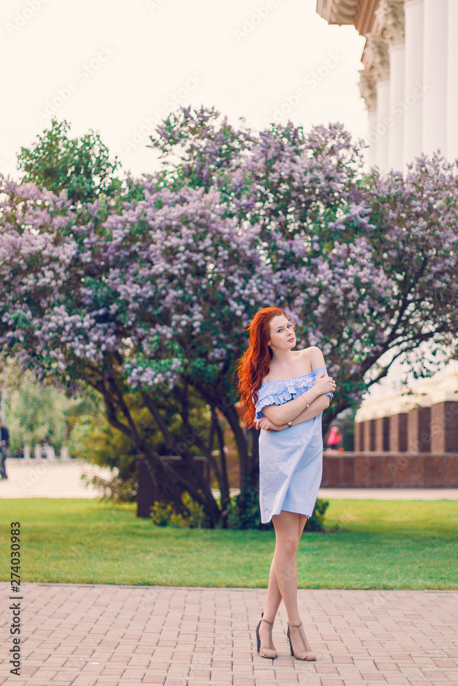 Red-haired Model posing in the summer in a dress of blooming lilacs.