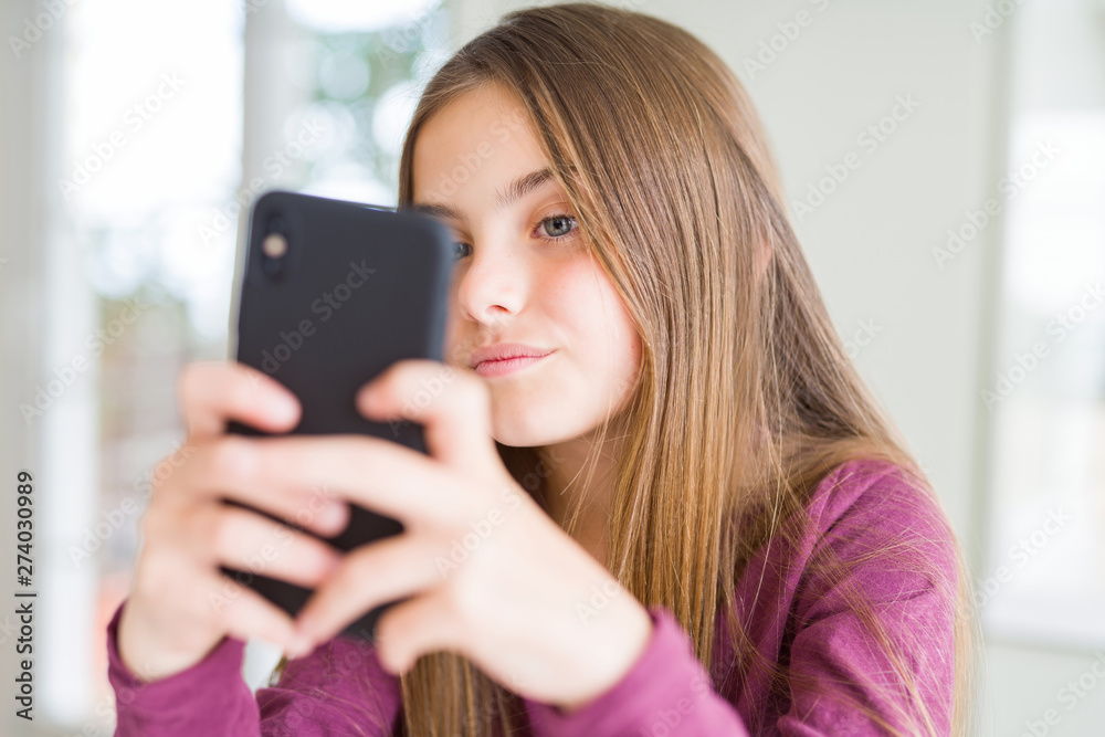 Beautiful young girl kid sending a message using smartphone with a confident expression on smart face thinking serious Beautiful young girl kid sending a message using smartphone with a confident expression on smart face thinking serious