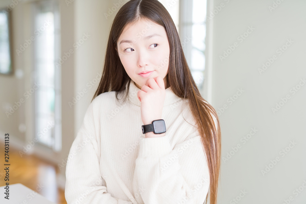 Beautiful Asian woman wearing casual sweater with hand on chin thinking about question, pensive expression. Smiling with thoughtful face. Doubt concept. Beautiful Asian woman wearing casual sweater with hand on chin thinking about question, pensive expression. Smiling with thoughtful face. Doubt concept.