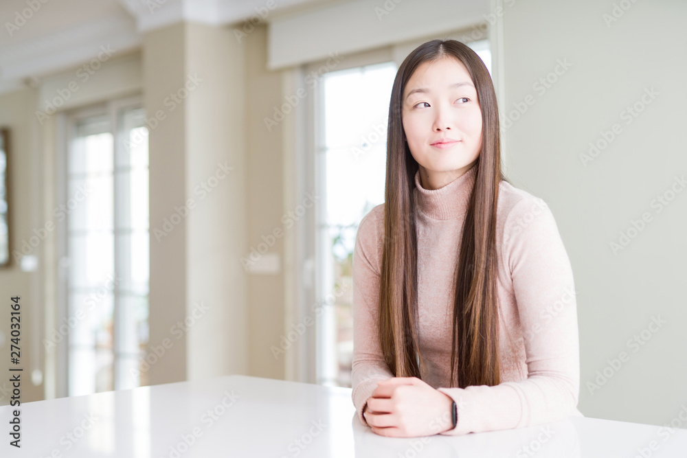 Beautiful Asian woman wearing casual sweater on white table smiling looking side and staring away thinking. Beautiful Asian woman wearing casual sweater on white table smiling looking side and staring away thinking.
