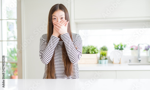 Beautiful Asian woman wearing stripes sweater shocked covering mouth with hands for mistake. Secret concept.