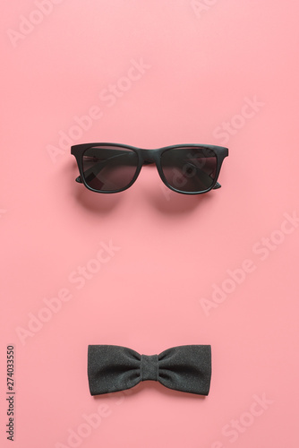 Black stylish sunglasses and bow tie on pink background. Flat lay. Minimal style concept