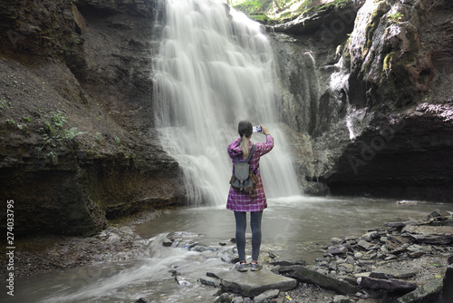 Girl in bright coat photographs waterfall with a phone photo