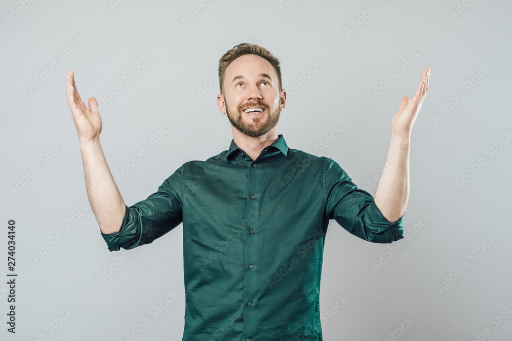 Fototapeta premium Joyful young man raising arms and looking up