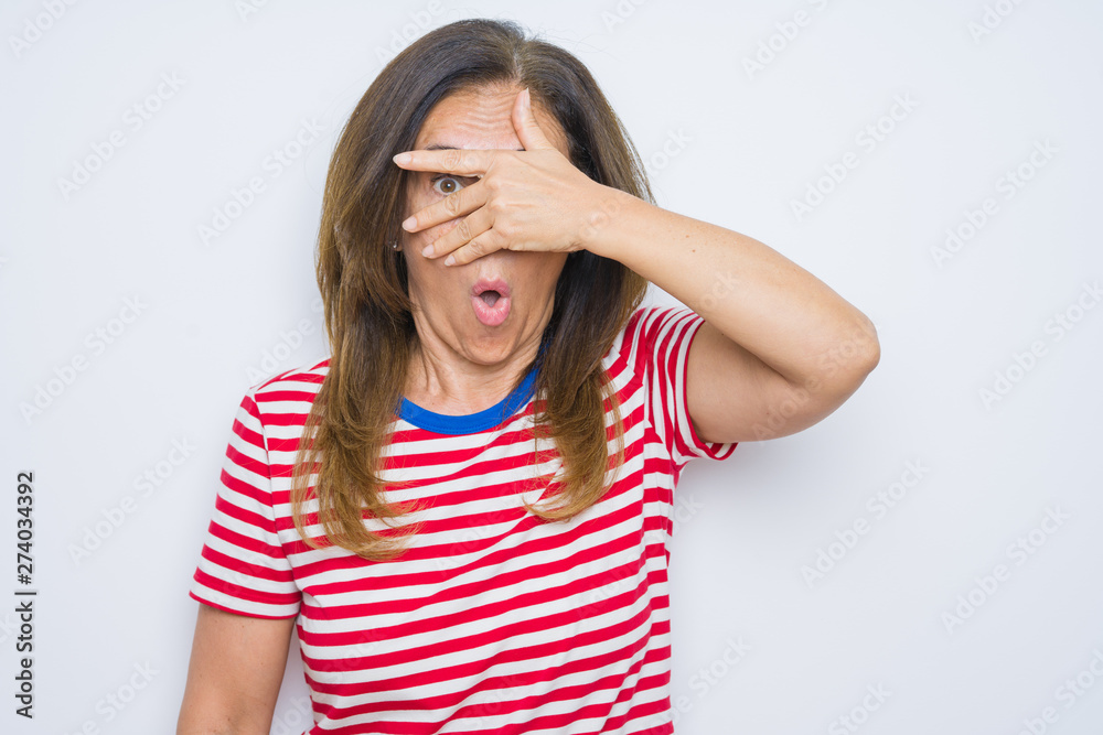 Middle age senior woman standing over white isolated background peeking in shock covering face and eyes with hand, looking through fingers with embarrassed expression. Middle age senior woman standing over white isolated background peeking in shock covering face and eyes with hand, looking through fingers with embarrassed expression.
