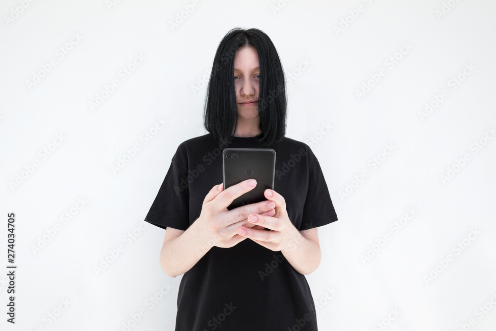 The girl in a black dress and with black hair with a smartphone in her hands on a white background. The girl is watching a video on a mobile phone The girl in a black dress and with black hair with a smartphone in her hands on a white background. The girl is watching a video on a mobile phone