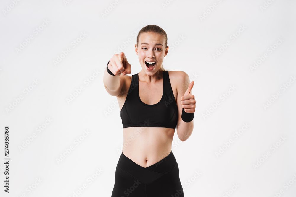 Image of nice amazed woman wearing tracksuit pointing finger at camera and showing thumb up