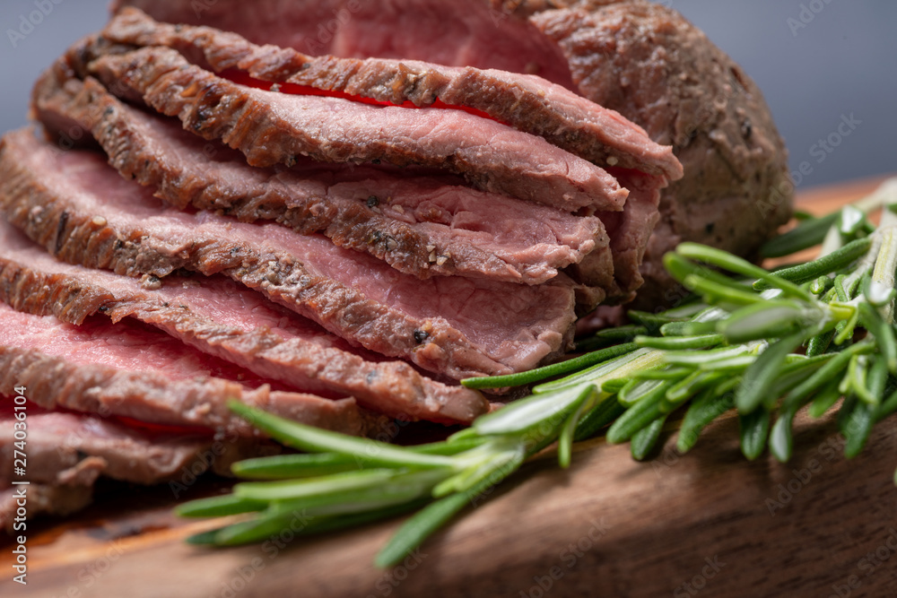 Sliced Grass Fed juicy Corn Roast Beef garnished with Rosemary Fresh Herb on natural wood cutting board.