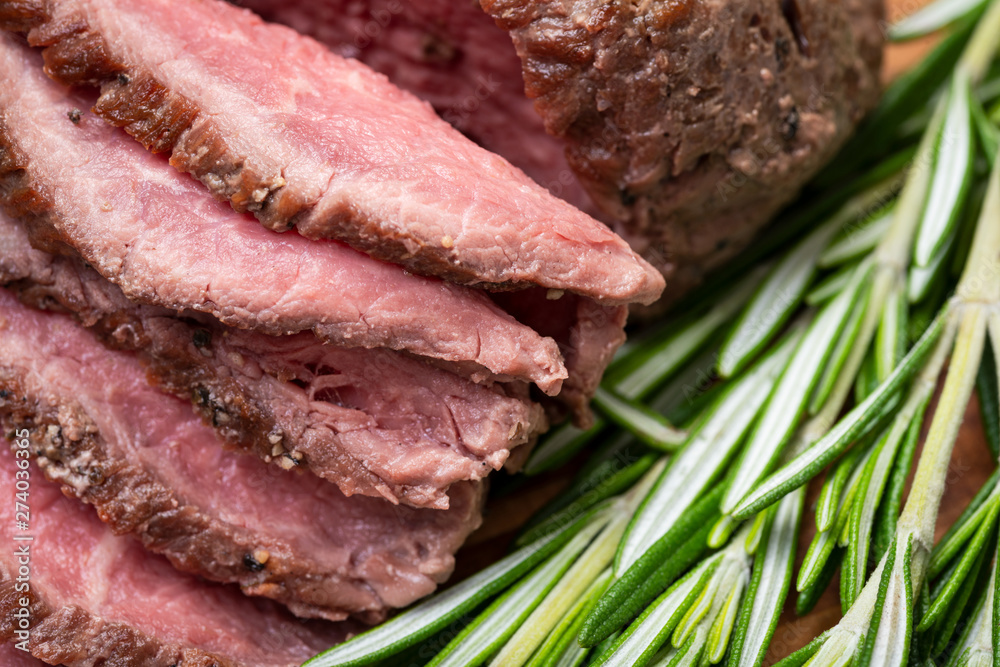 Sliced Grass Fed juicy Corn Roast Beef garnished with Rosemary Fresh Herb on natural wood cutting board. Sliced Grass Fed juicy Corn Roast Beef garnished with Rosemary Fresh Herb on natural wood cutting board.