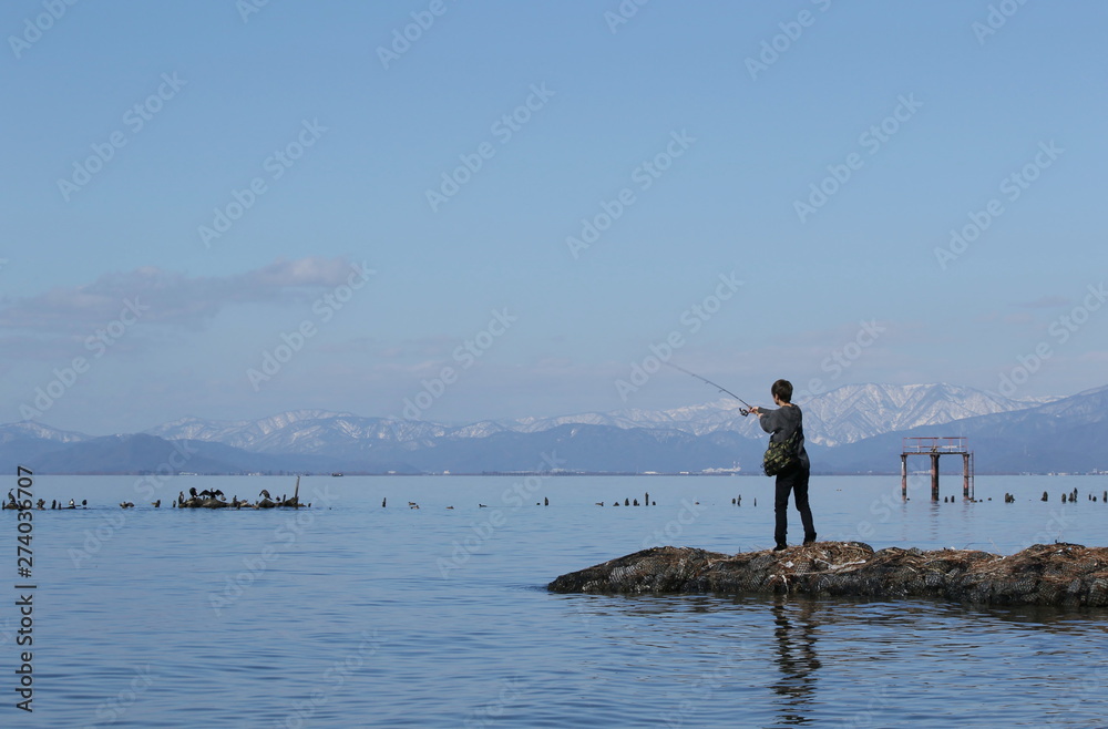 晴天の琵琶湖岸で釣りをする若者