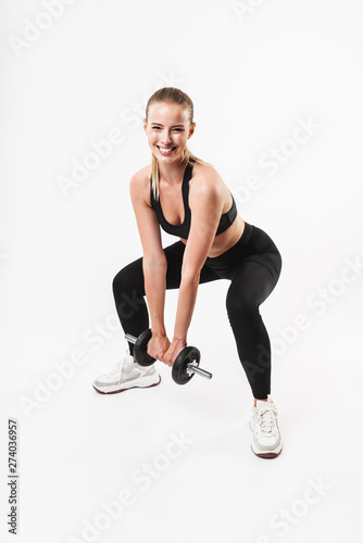 Image of happy strong woman wearing tracksuit smiling while lifting dumbbell during workout