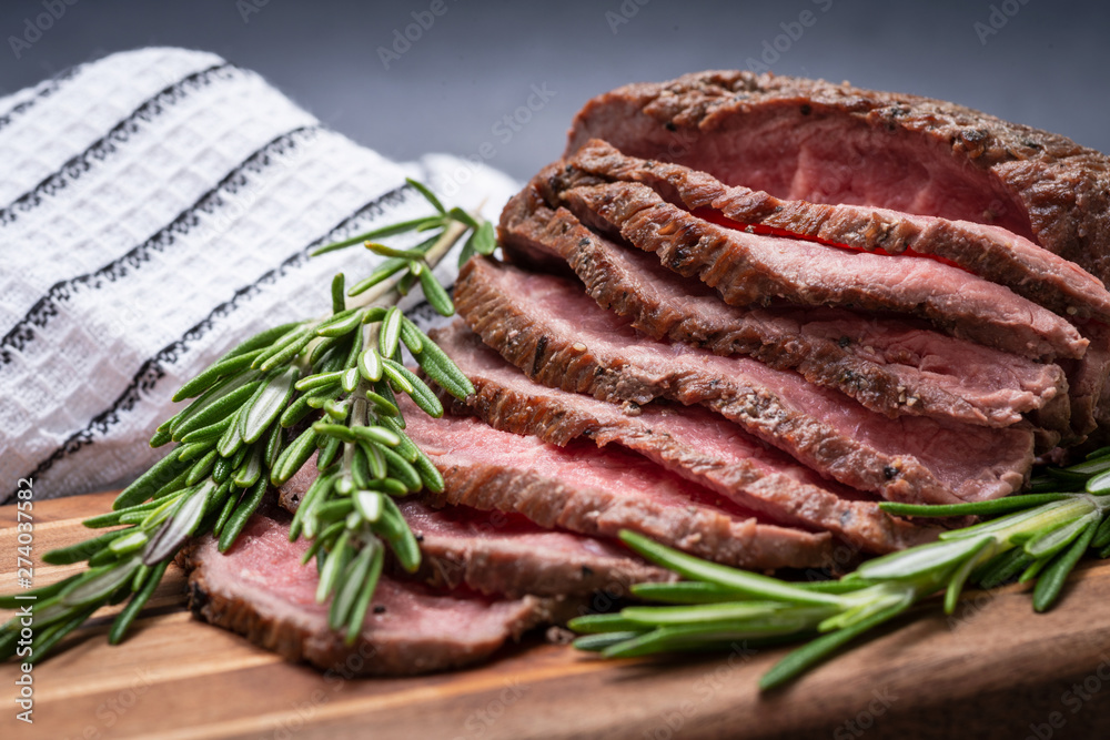 Sliced Grass Fed juicy Corn Roast Beef garnished with Rosemary Fresh Herb on natural wood cutting board.