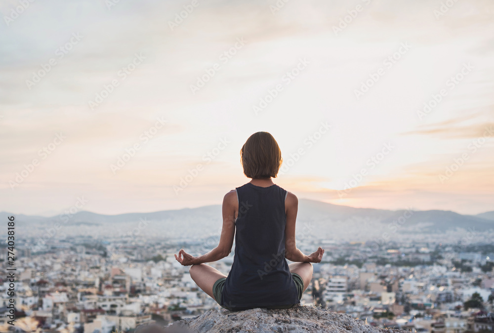 Young woman practicing yoga outdoors at sunset with a big city at the background. Harmony and meditation concept. Healthy lifestyle