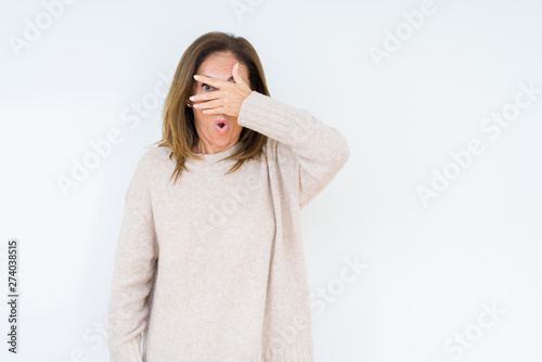 Beautiful middle age woman over isolated background peeking in shock covering face and eyes with hand, looking through fingers with embarrassed expression.