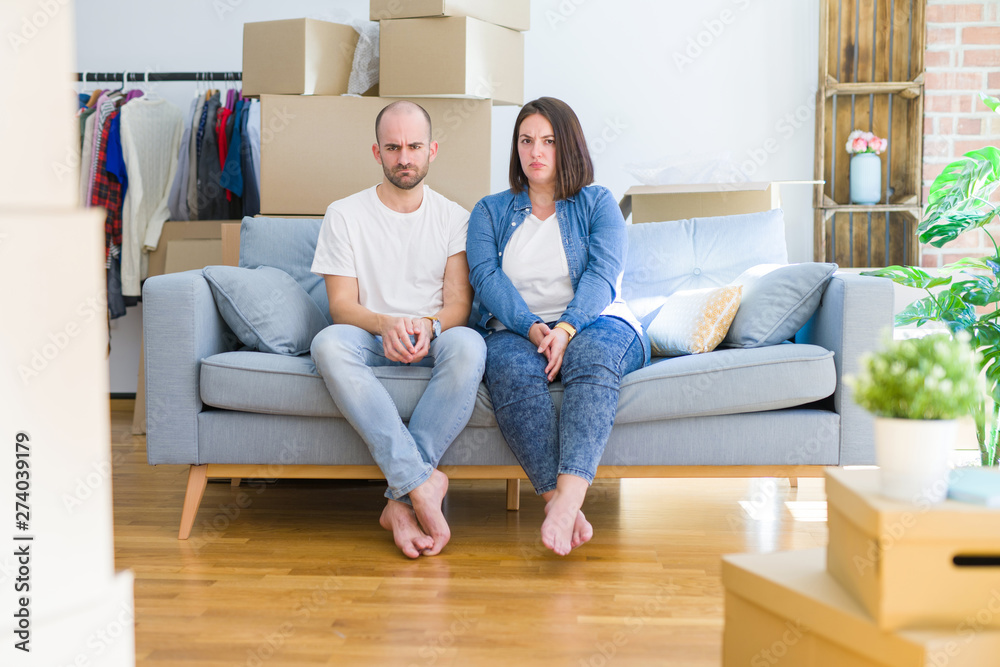 Young couple sitting on the sofa arround cardboard boxes moving to a new house skeptic and nervous, frowning upset because of problem. Negative person. Young couple sitting on the sofa arround cardboard boxes moving to a new house skeptic and nervous, frowning upset because of problem. Negative person.