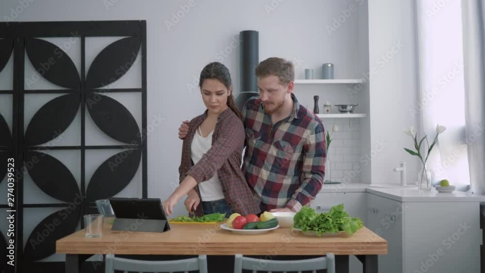 portrait of smiling loving couple in cuisine, happy girl with guy prepares healthy food for dinner with fresh vegetables on kitchen table using tablet with video recipe portrait of smiling loving couple in cuisine, happy girl with guy prepares healthy food for dinner with fresh vegetables on kitchen table using tablet with video recipe