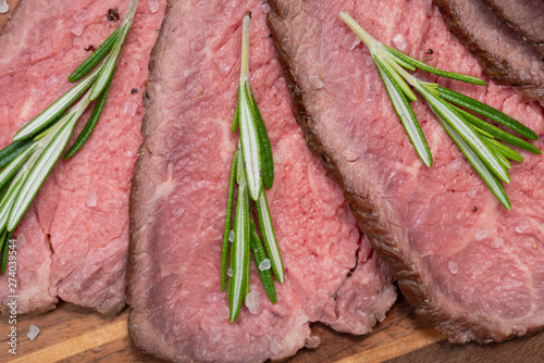 Sliced Grass Fed juicy Corn Roast Beef garnished with Rosemary Fresh Herb on natural wood cutting board.