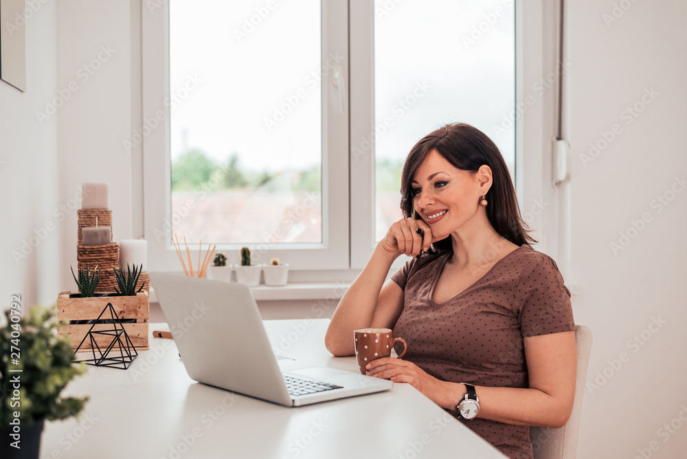 Portrait of a beautiful woman enjoying morning coffee and looking at laptop.