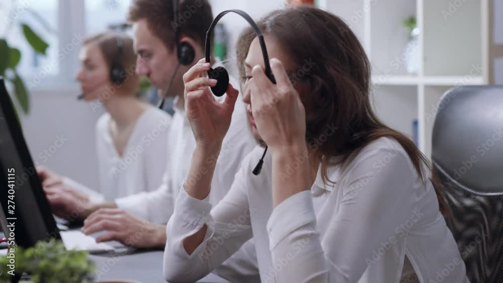 Bored attractive female operator working online listening a conversation of a ccustomer with headset at office, ends the talk, puts off the headset and sighs with a relief. Exhausted, bad mood