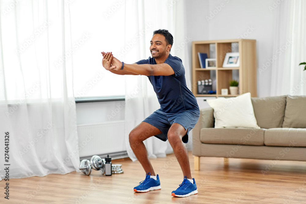© Syda Productions - sport and healthy lifestyle concept - smiling indian man with fitness tracker exercising and doing squats at home © Syda Productions - sport and healthy lifestyle concept - smiling indian man with fitness tracker exercising and doing squats at home