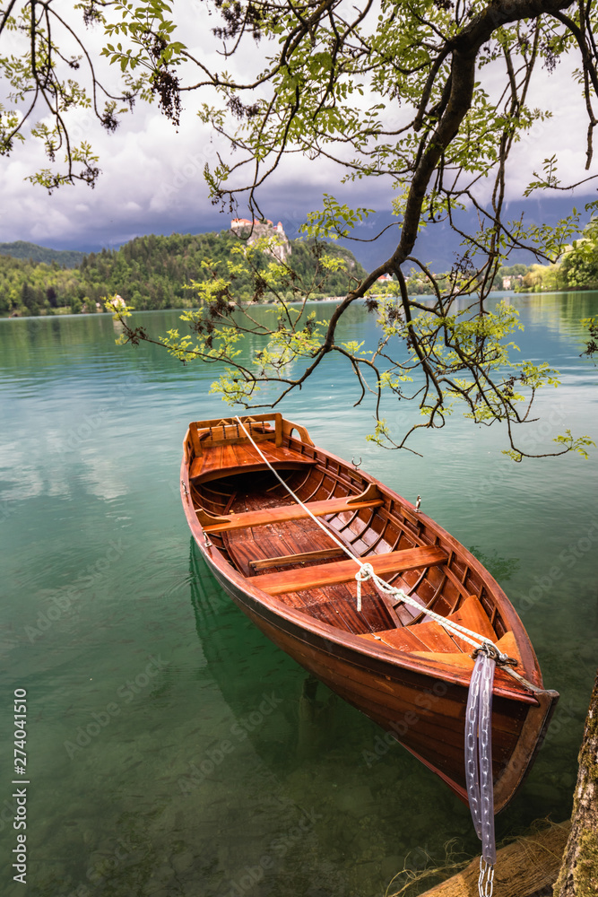 scenic view on beautiful wooden flat rowing boat on lake bled beside attached to a tree, slovenia, go green concept