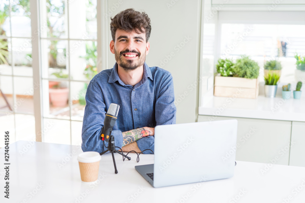 Young man recording podcast using microphone and laptop happy face smiling with crossed arms looking at the camera. Positive person.