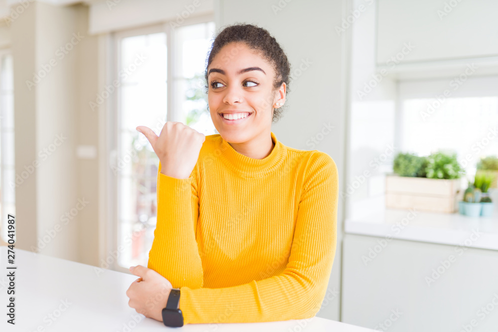 Beautiful young african american woman with afro hair smiling with happy face looking and pointing to the side with thumb up. Beautiful young african american woman with afro hair smiling with happy face looking and pointing to the side with thumb up.