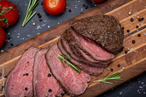 Sliced Grass Fed juicy Corn Roast Beef garnished with Tomatoes, Fresh Rosemary Herb and Rainbow Peppercorns on natural wooden cutting board. © bjphotographs