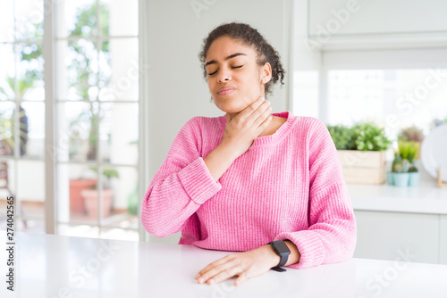 Beautiful african american woman with afro hair wearing casual pink sweater Touching painful neck, sore throat for flu, clod and infection