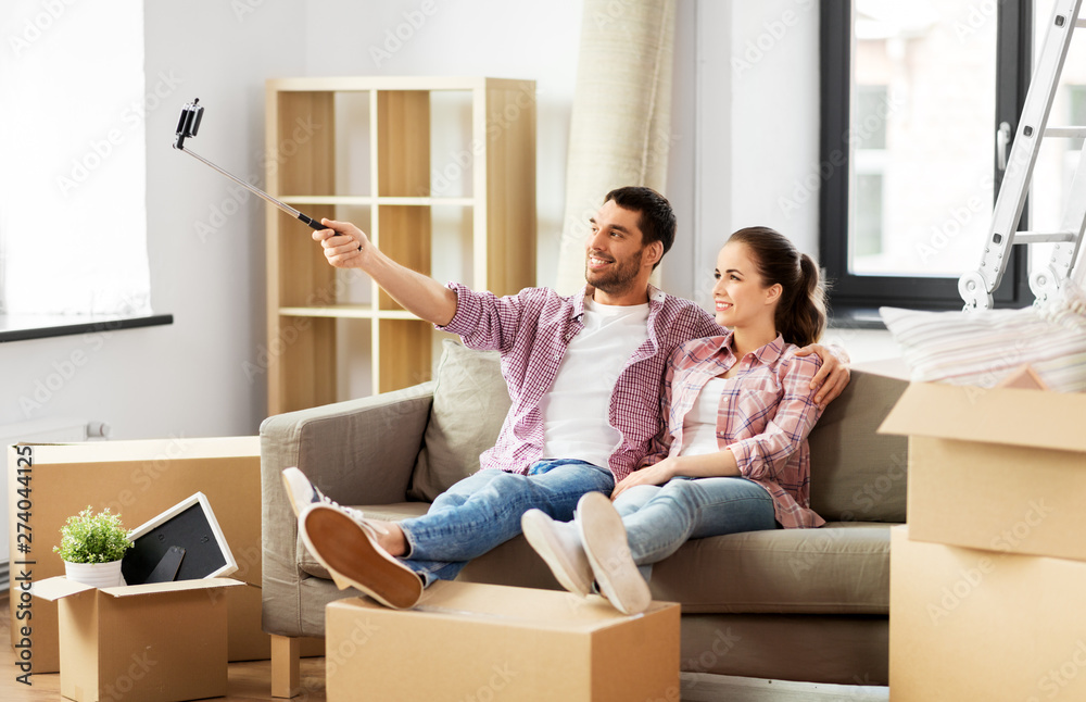 moving, repair and real estate concept - smiling couple taking picture by selfie stick at new home moving, repair and real estate concept - smiling couple taking picture by selfie stick at new home
