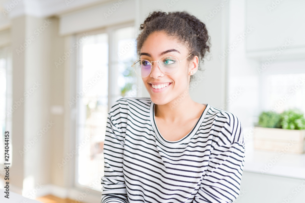 Beautiful young african american woman with afro hair wearing glasses smiling looking side and staring away thinking.