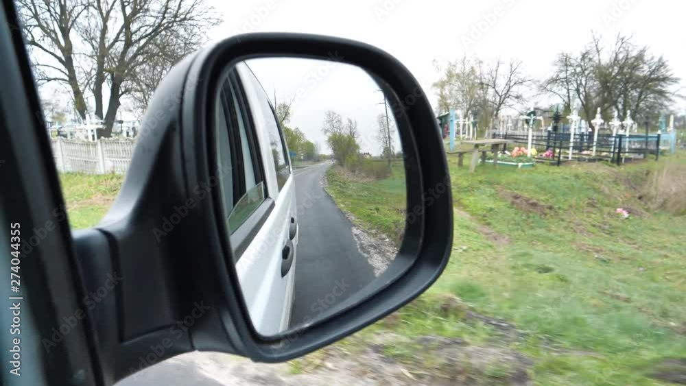 Car rides along the graveyard. View on the side mirror of the car Car rides along the graveyard. View on the side mirror of the car