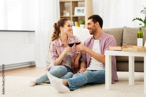 leisure, celebration and valentines day concept - happy couple drinking red wine at home