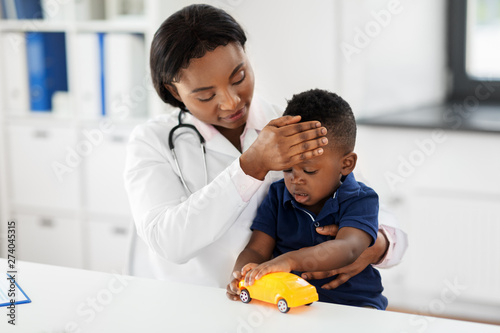 medicine, healtcare, pediatry and people concept - happy african american female doctor or pediatrician measuring baby's temperature by hand on medical exam at clinic